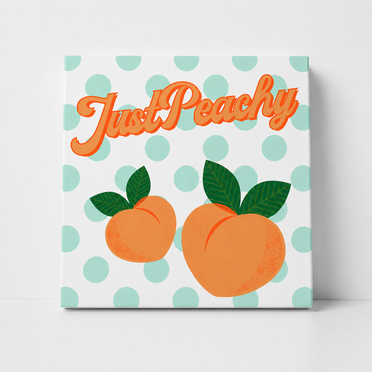 A square decorative sign or canvas print featuring the phrase 'Just Peachy' in orange script above two peach illustrations with green leaves, set against a white background with light mint green polka dots.