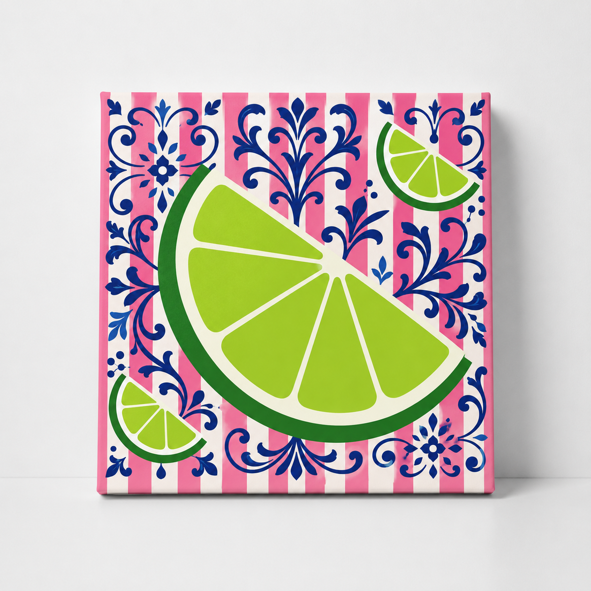 A square decorative tile or coaster featuring a vibrant lime wedge and smaller lime slices over a pink and white striped background with a blue damask pattern, shown standing upright against a light gray wall.